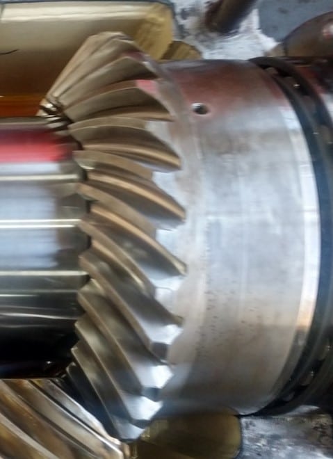 Close-up of a metal bevel gear with helical teeth, highlighting detailed machining and polished surfaces. This precision component is essential in industrial gearbox rebuild and larger mechanical assemblies.