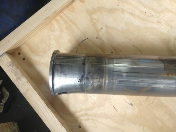 A metal cylinder with a deformed end and visible scratches lies on a wooden crate, suggesting the need for industrial gearbox rebuild or emergency gearbox repair due to clear signs of wear or damage.