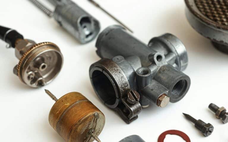 Assorted mechanical parts, including metal cylinders, screws, and a brass float, are laid out on a white surface—components often used in industrial gearbox repair or rebuild services.