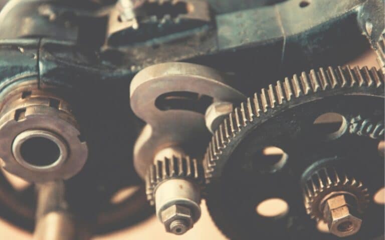 Close-up view of interlocking metal gears and mechanical parts in a machine, showcasing details of the cogs and bolts. The image captures the essence of industrial gearbox rebuild with a vintage, slightly muted color tone.